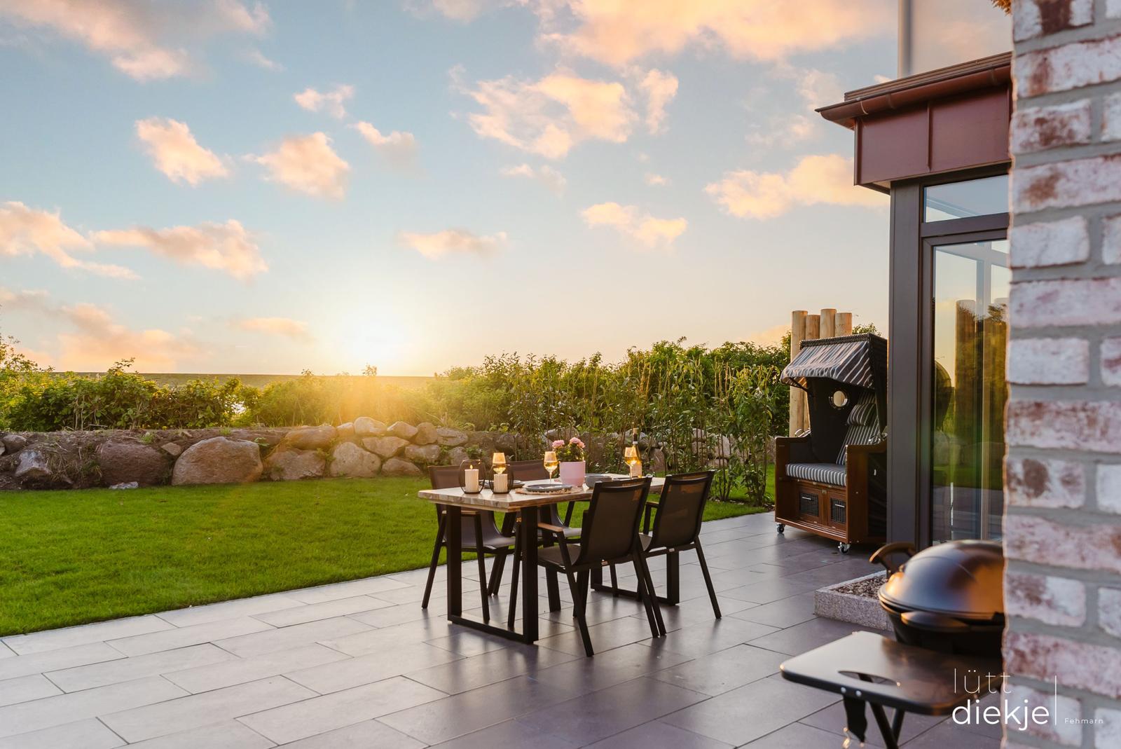 Terrasse mit Tisch, Stühlen, Grill und Liege im Sonnenuntergang.