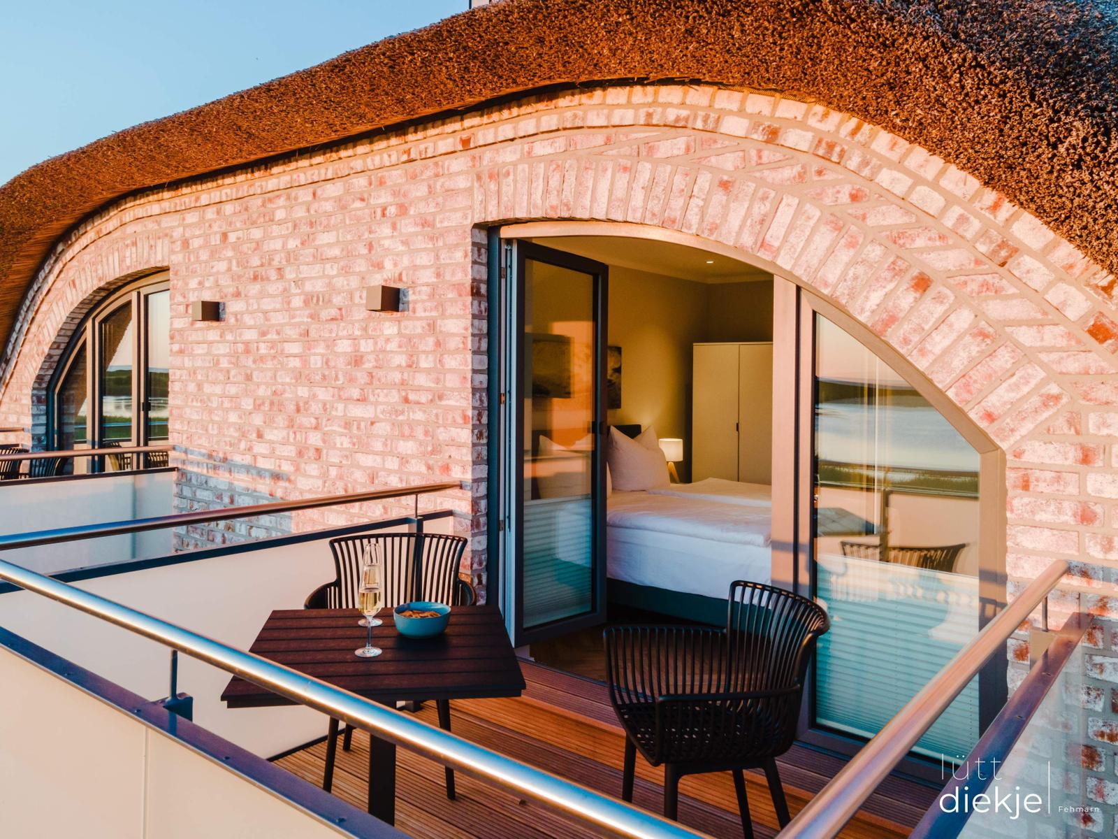 Terrasse mit Tisch und Stühlen. Durch Glastür ist Schlafzimmer mit Bett sichtbar.