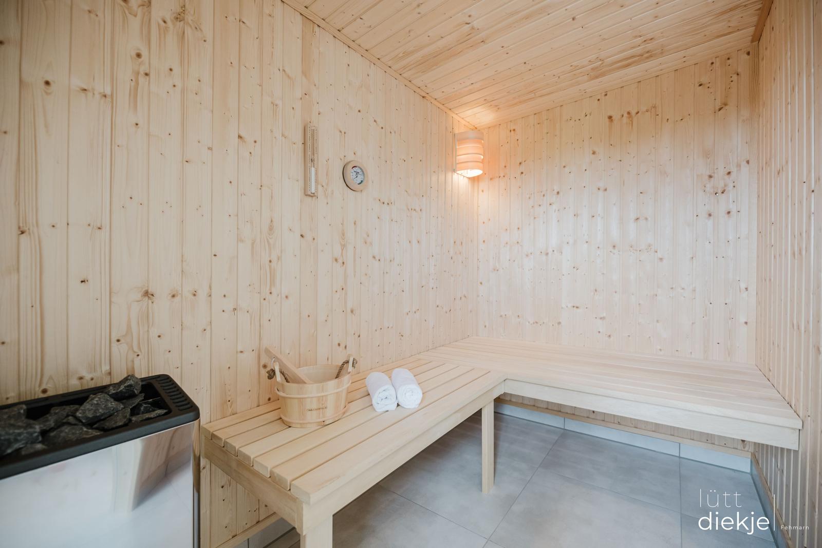 Sauna mit Holzbank, Thermometer und Wasserbucket.