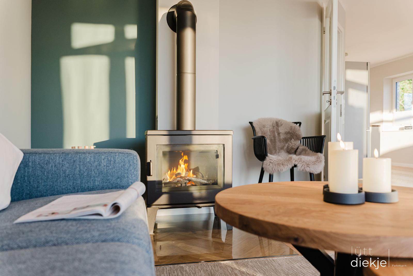 Ein Kamin mit brennendem Holz, ein Sofa und ein runder Tisch mit Kerzen.