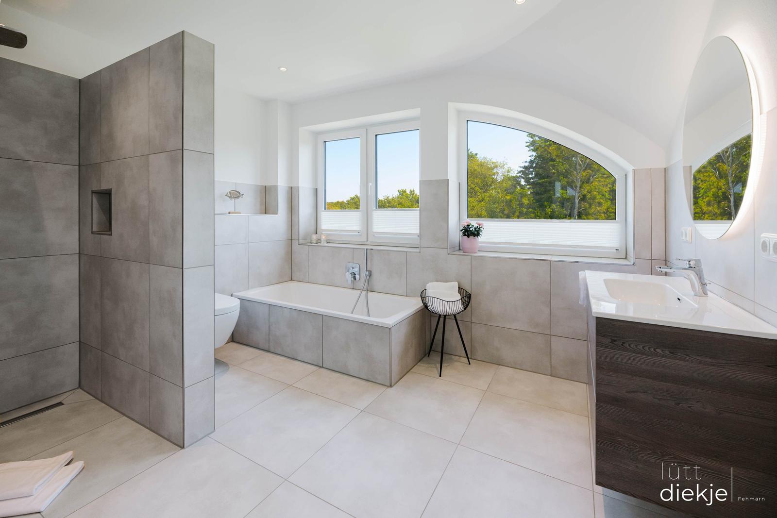 Bad mit Badewanne, Dusche und Waschbecken. Fenster mit Blick auf Bäume.