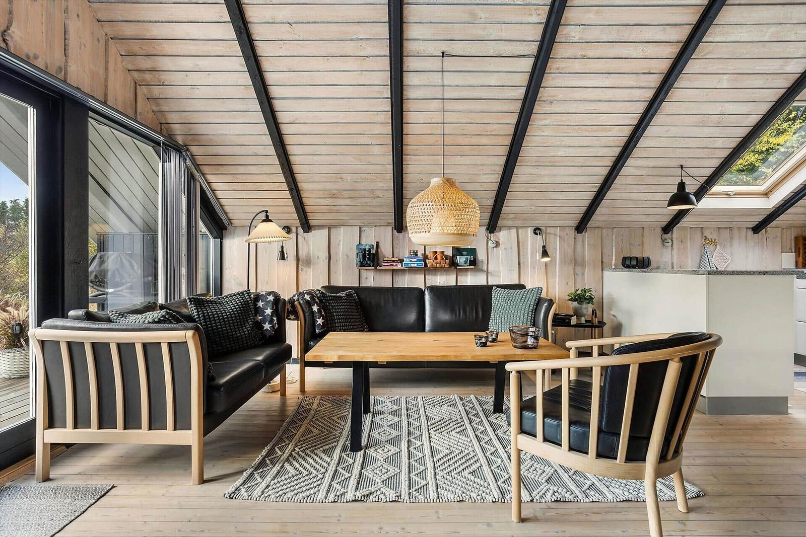 Living room with wooden ceiling, sofa, chairs, table, and rug.