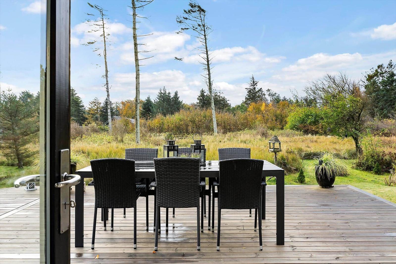 Deck with dining table and chairs, view of forest and meadow.