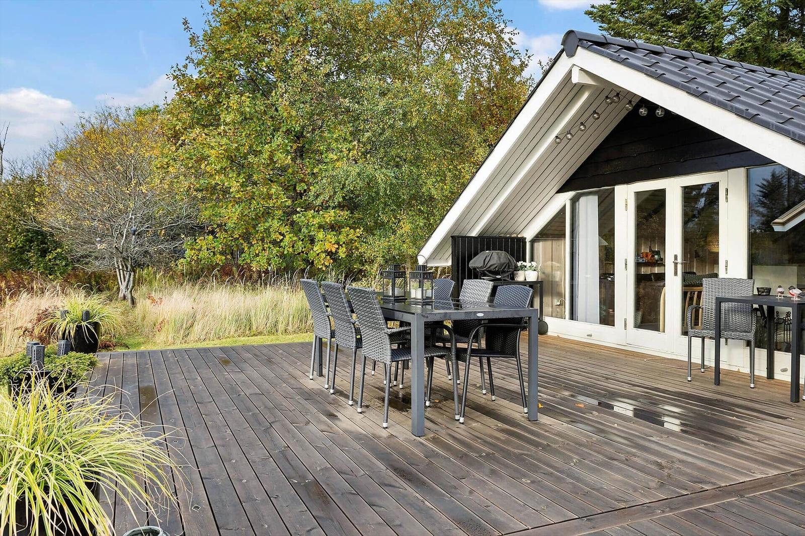 Deck with table and chairs in front of a house with glass doors.