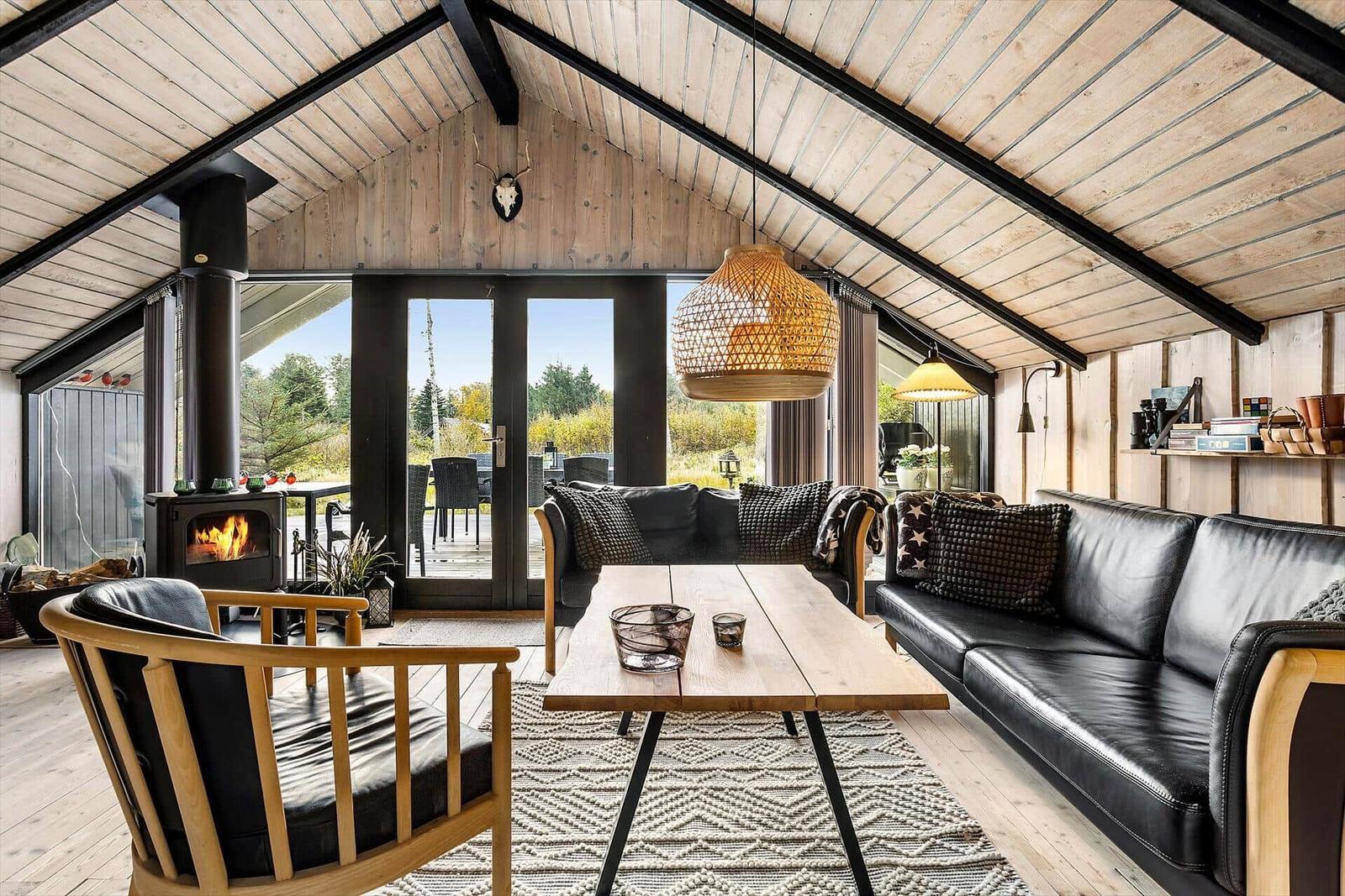 Living room with fireplace, sofa, and table. Wooden ceiling and large windows.