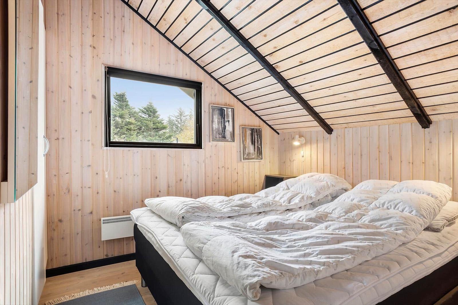 Bedroom with wooden walls, roof window, and bed