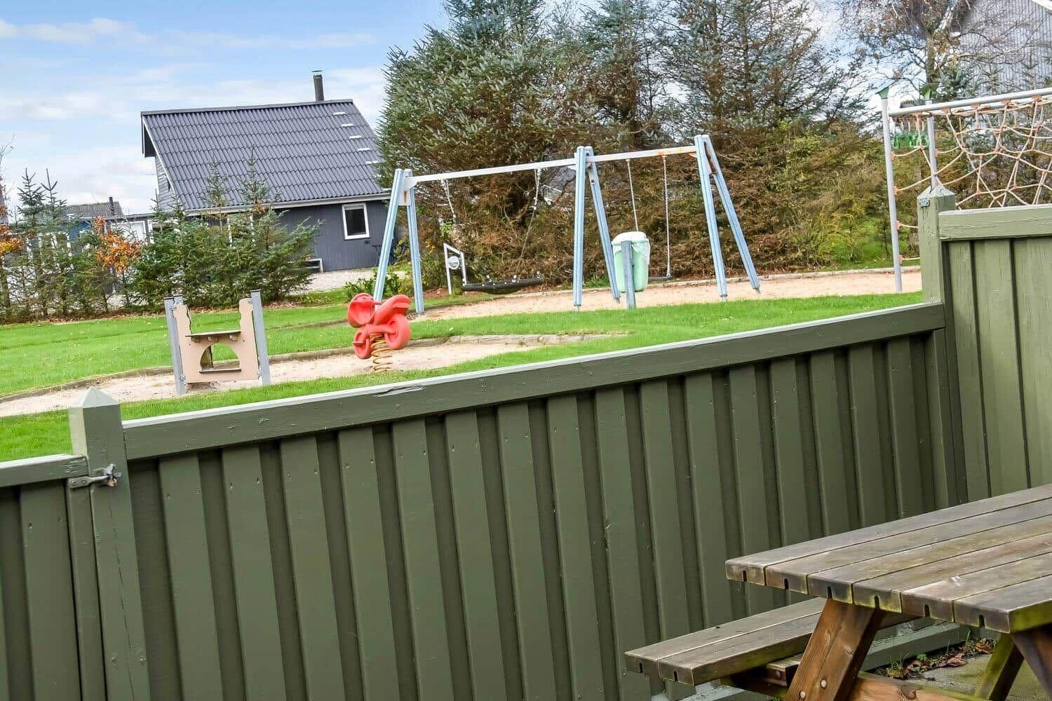 Hinterhof mit Spielplatz, Holztisch und grünem Zaun. Im Hintergrund Haus und Bäume.