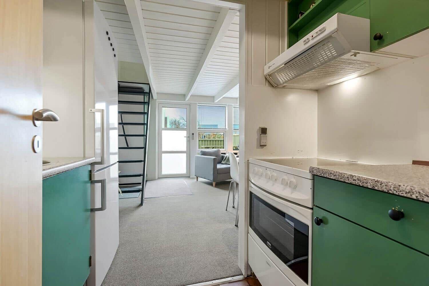 Küche mit grünen Schränken und Blick in Wohnbereich mit Sofa und Treppe.