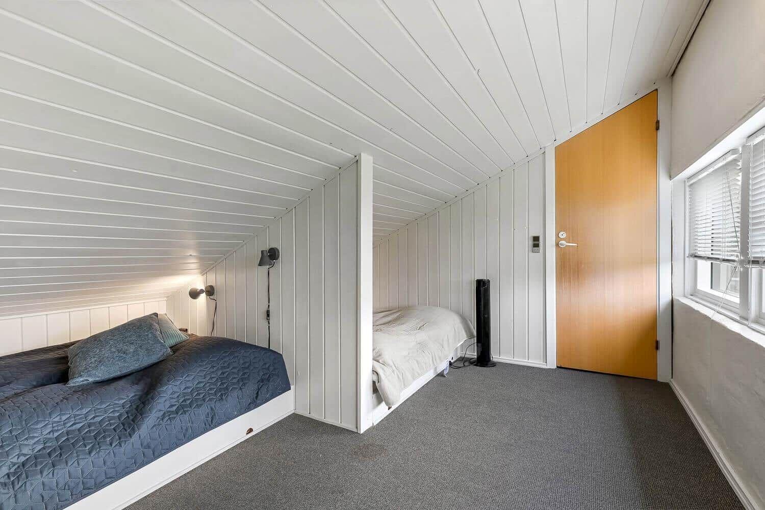 Zimmer mit zwei Betten, Holztür und Fenster mit Jalousie.