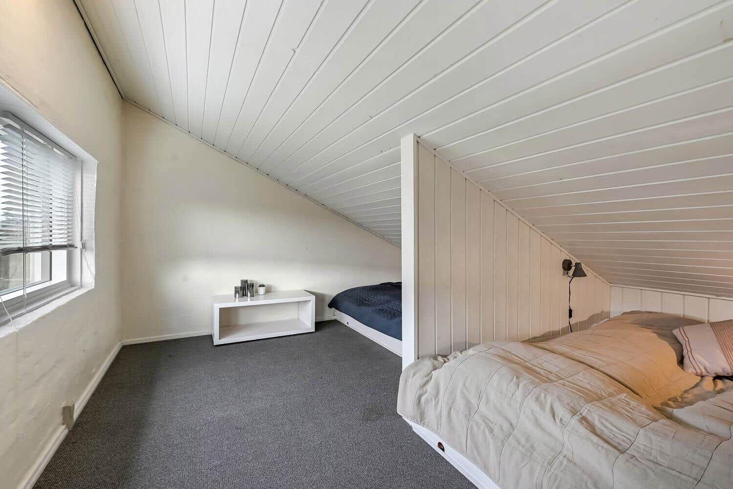 Zimmer mit zwei Betten, Fenster und weißem Schrank unter Dachschrägen.