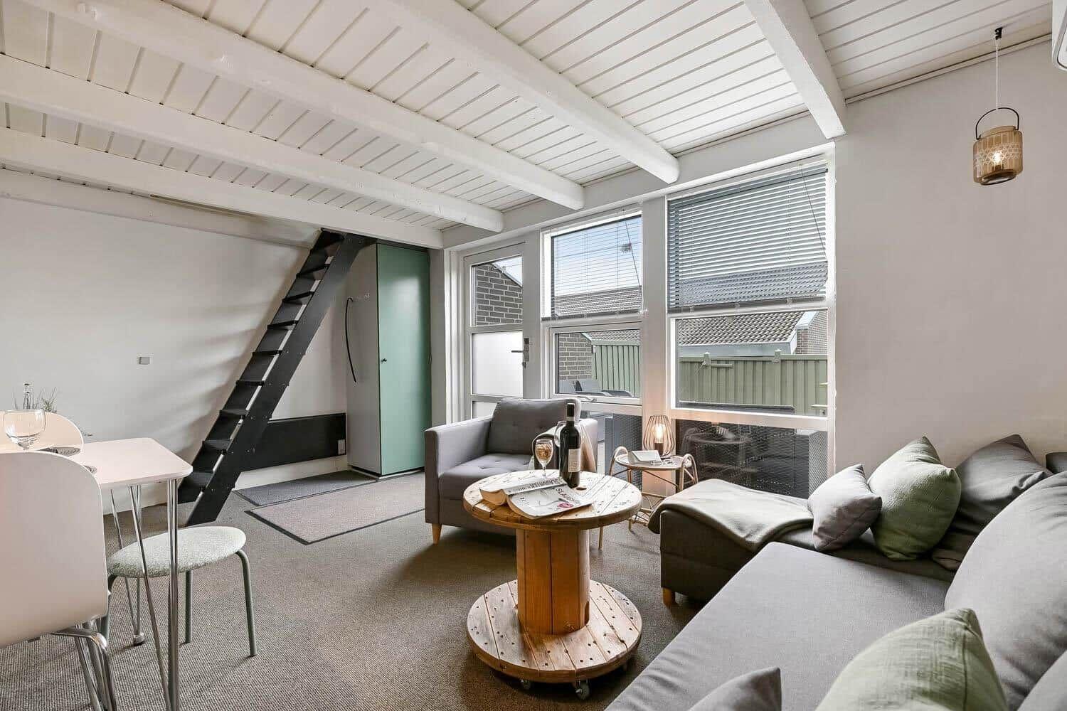 Wohnraum mit Sofa, Sitzgelegenheit und Tisch. Fenster und Dachschrägen sichtbar.