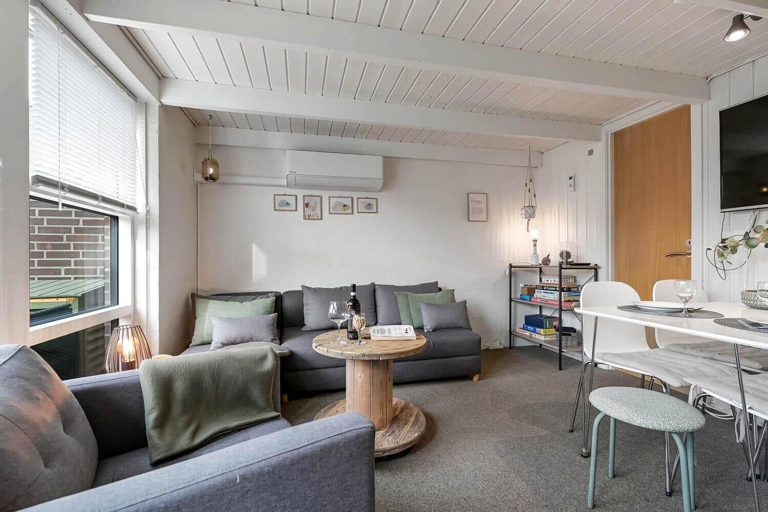 Wohn- und Essbereich mit Sofa, Tisch und Stühlen. Fenster, Decke und Wand sichtbar.