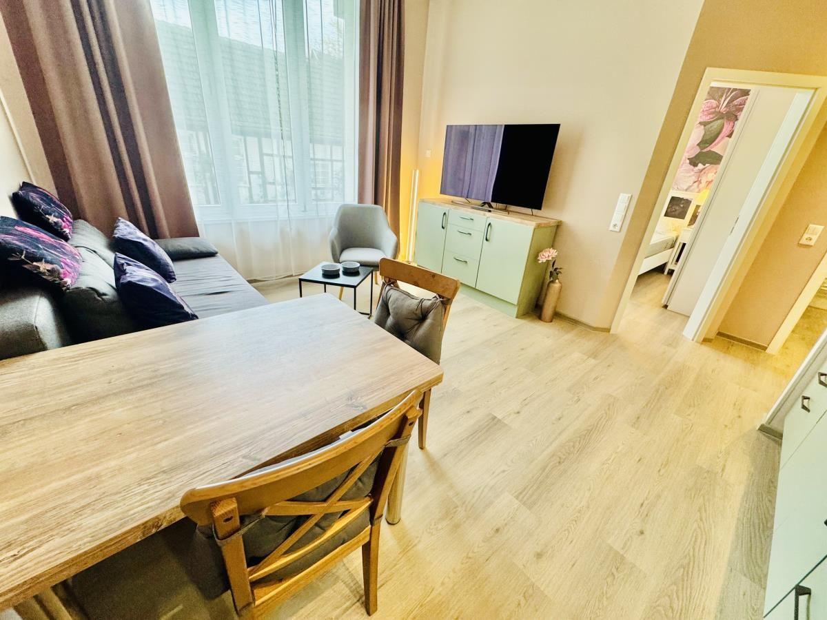Wohn- und Essbereich mit Sofa, TV und Holztisch.