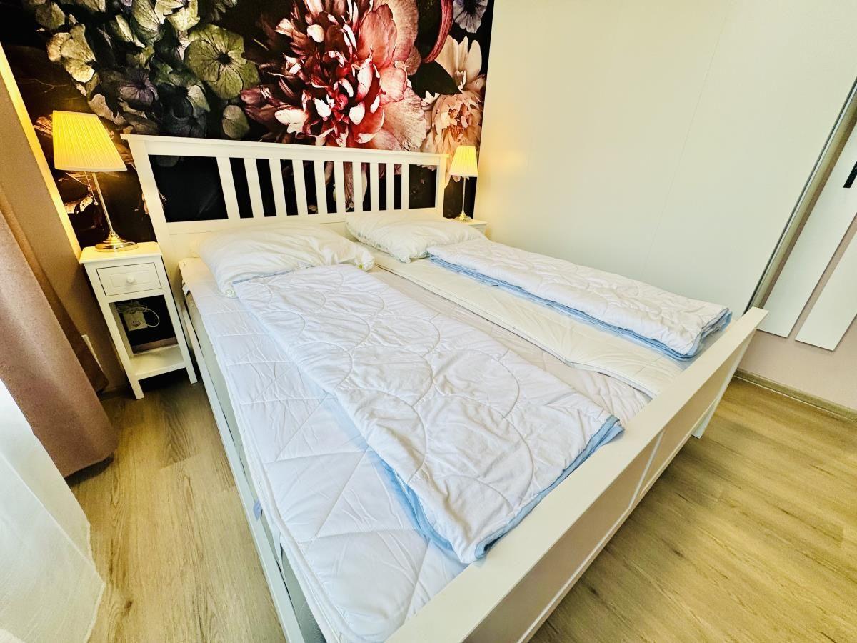 Schlafzimmer mit weißem Bett, floraler Wand und Nachttischen.