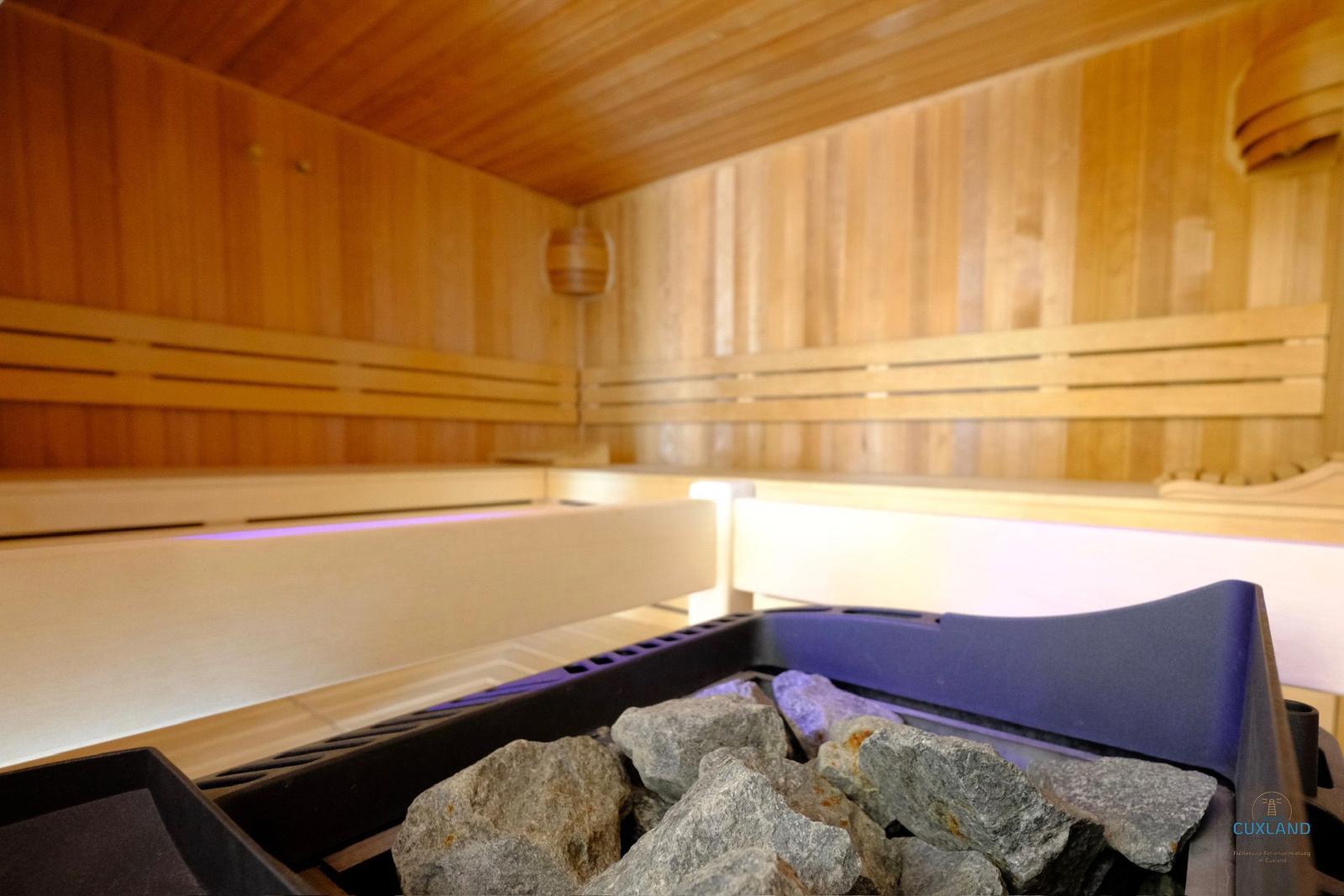 Sauna mit Holzwänden, Sitzbänken und Steinen im Vordergrund.