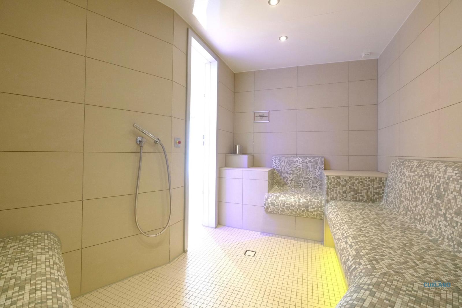 Dampfbad mit Sitzbänken, Dusche und Fliesenboden.