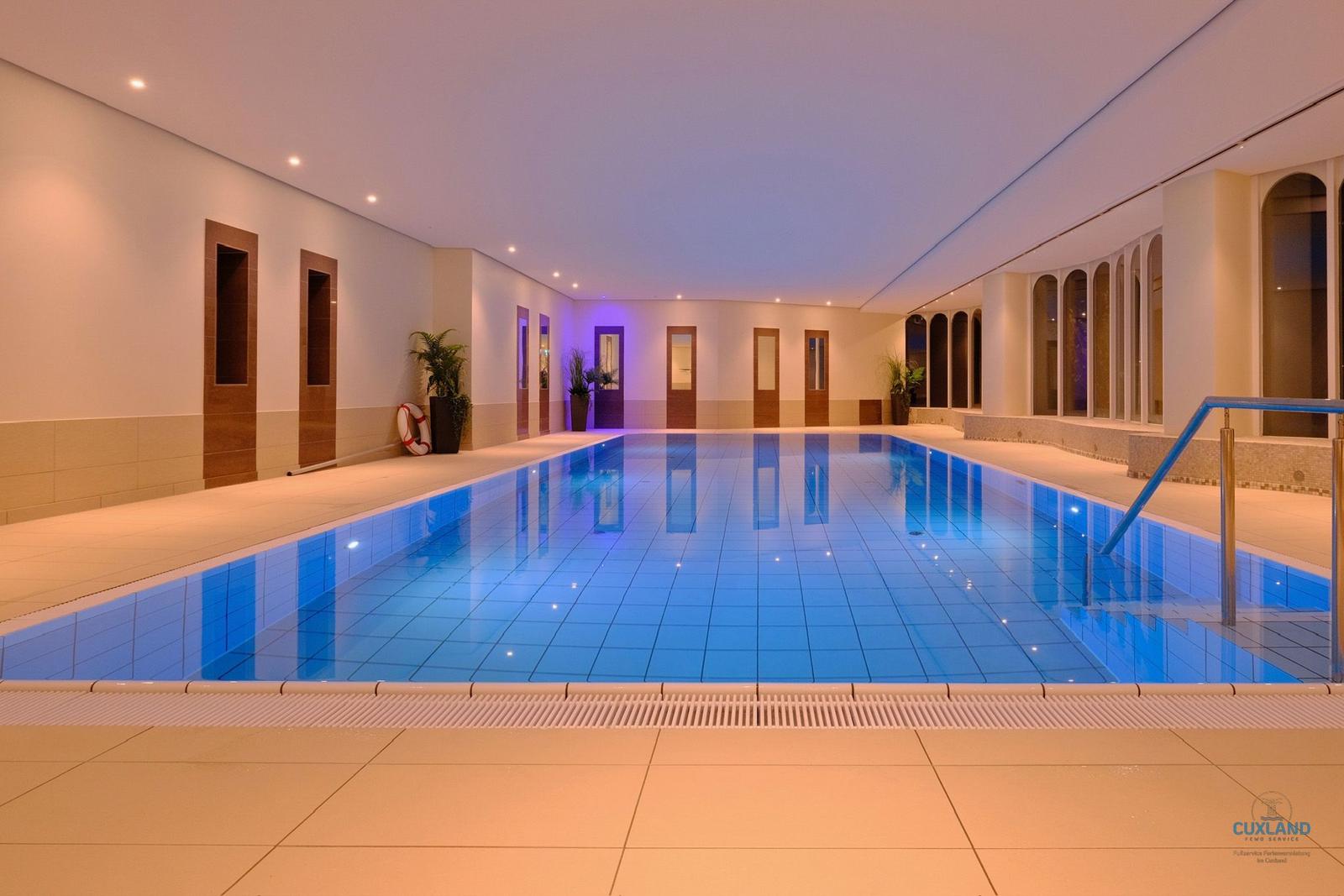 Innenpool mit blauer Beleuchtung und Holztüren entlang der Wände.