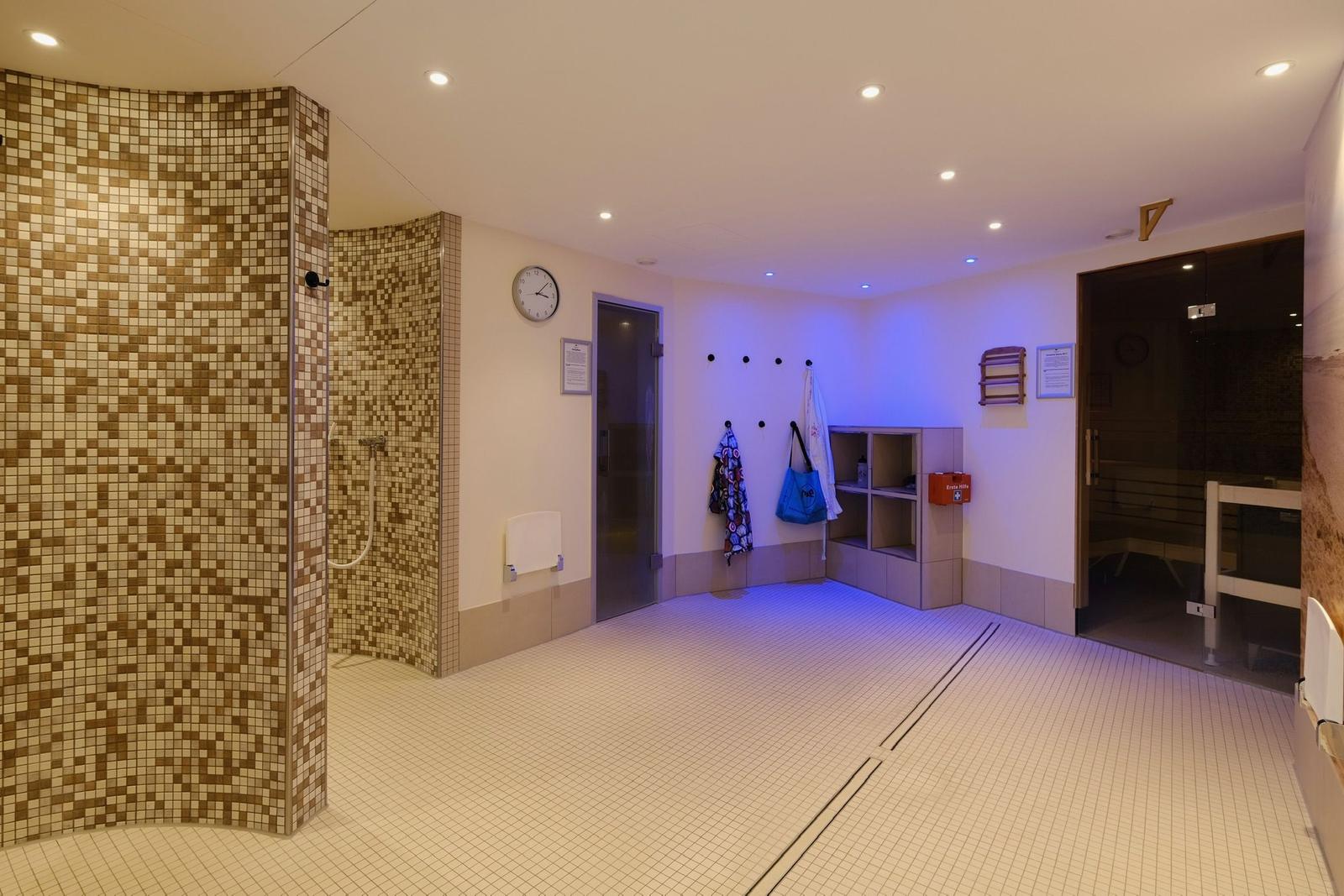 Duschkabine mit Mosaikwand, Sauna und Umkleidebereich mit Haken und Regal.