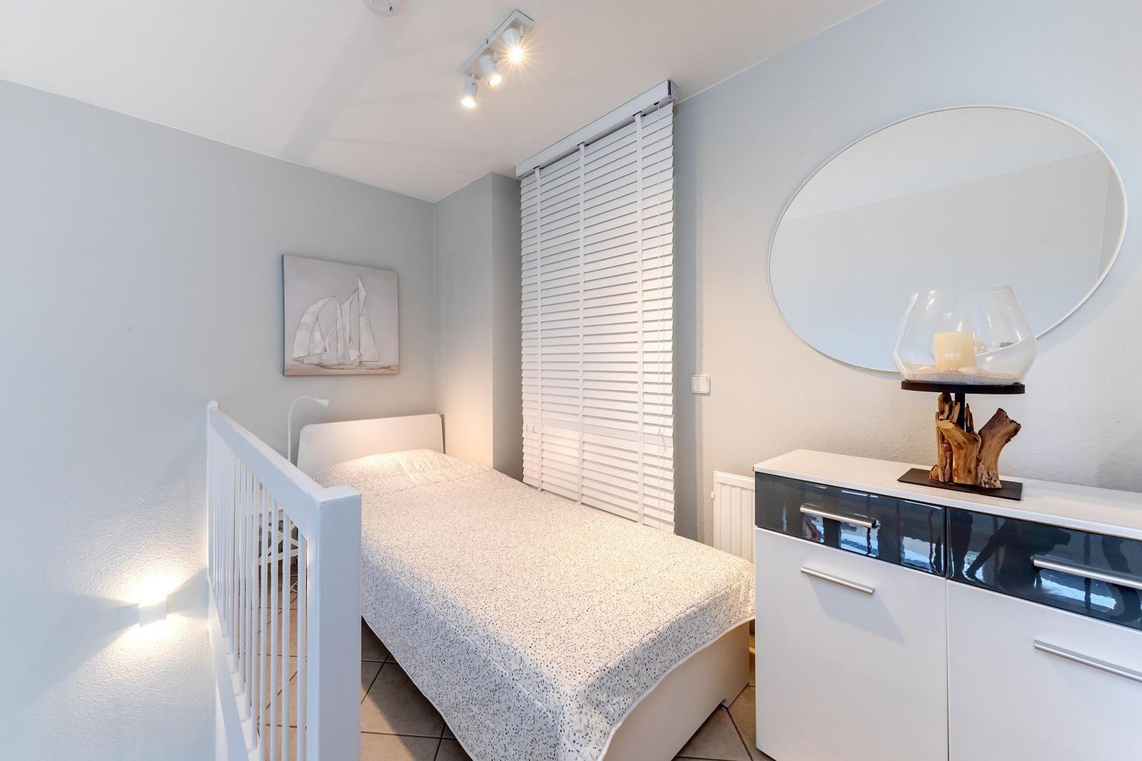 Ein Schlafzimmer mit Bett, Schrank und Wandspiegel. An der Wand hängt ein Bild.