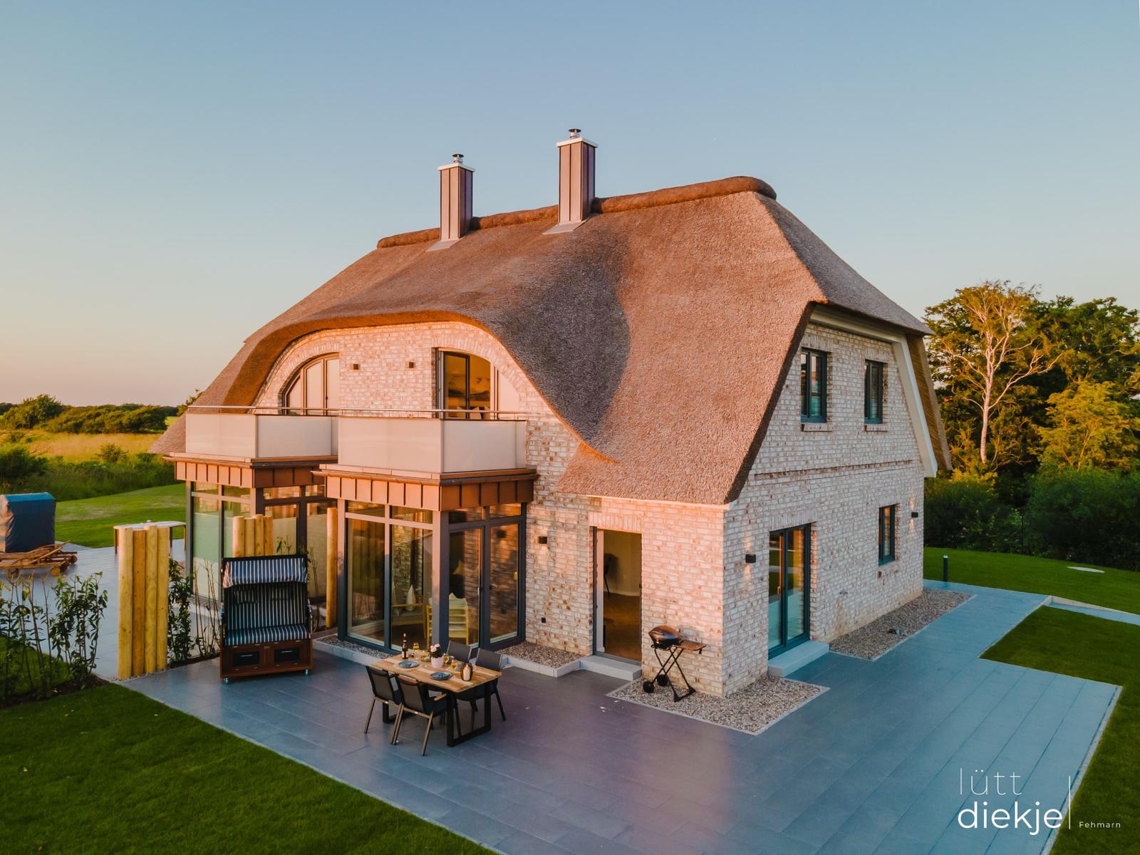 Modernes Haus mit Strohdach, Terrasse und Garten. Grill und Sitzgelegenheiten vorhanden.