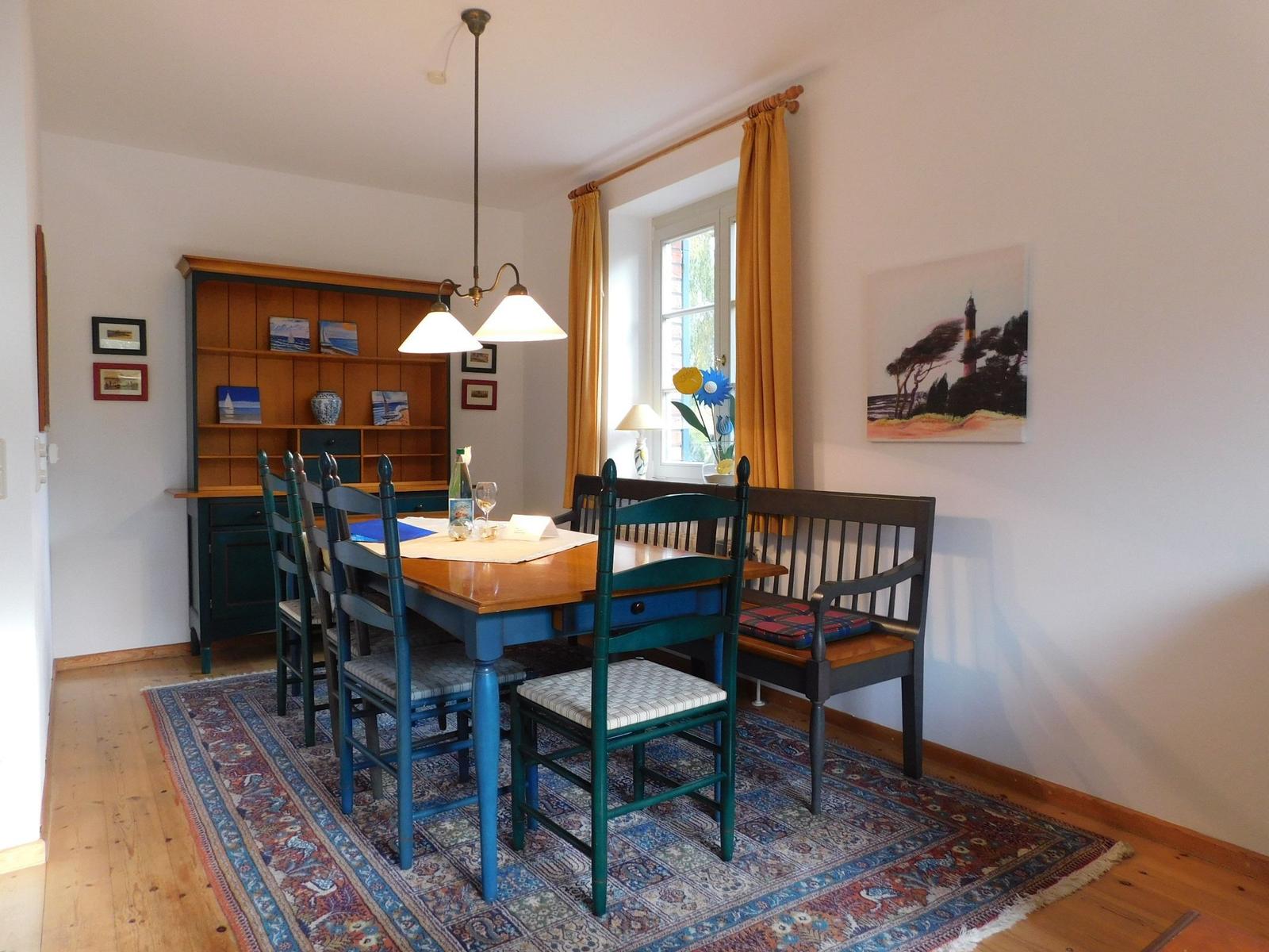 Esszimmer mit Holztisch, Stühlen und Regal. Fenster mit Vorhängen und Teppich.