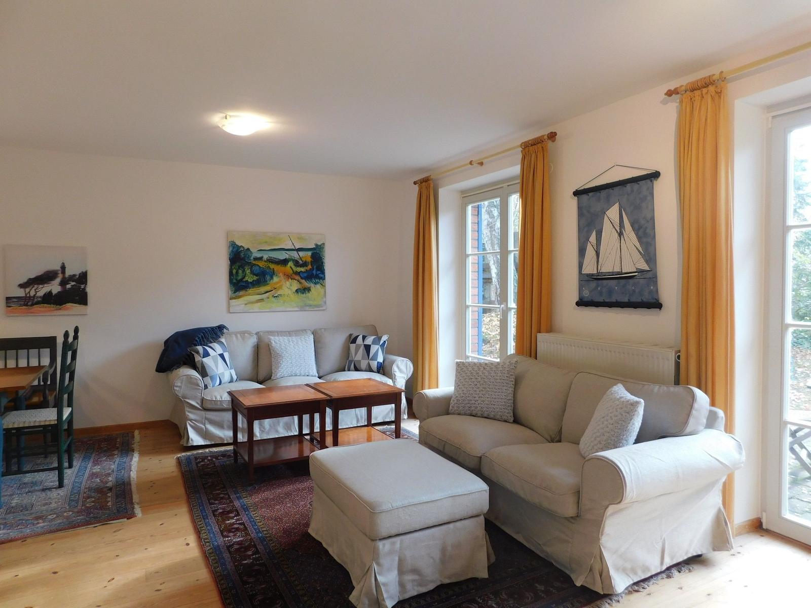 Wohnzimmer mit zwei Sofas, Tisch, Teppich und Fenstern mit Vorhängen.