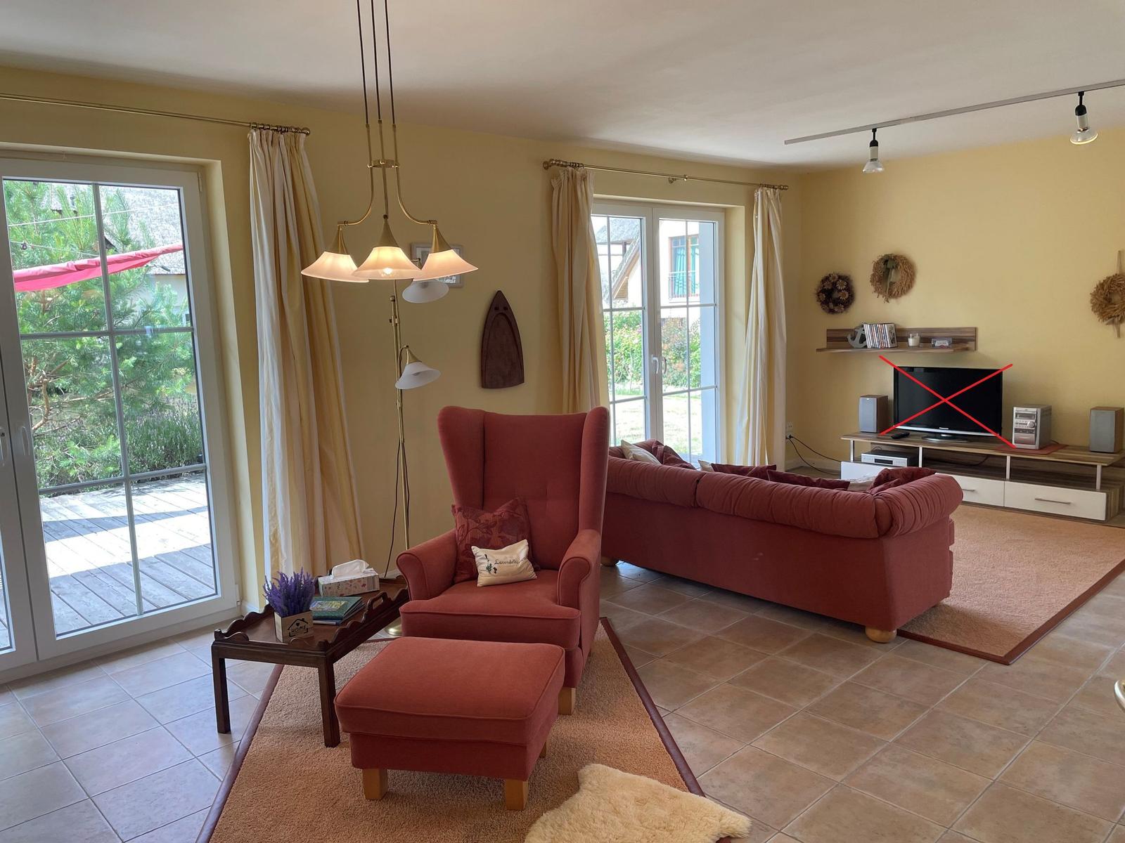 Wohnzimmer mit rotem Sofa, Sessel und Terrassentür. Fernseher auf Holzregal.