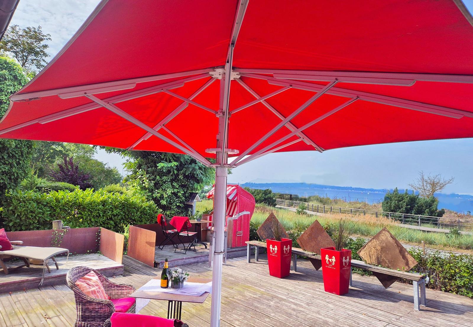Terrasse mit rotem Sonnenschirm und Blick aufs Meer.