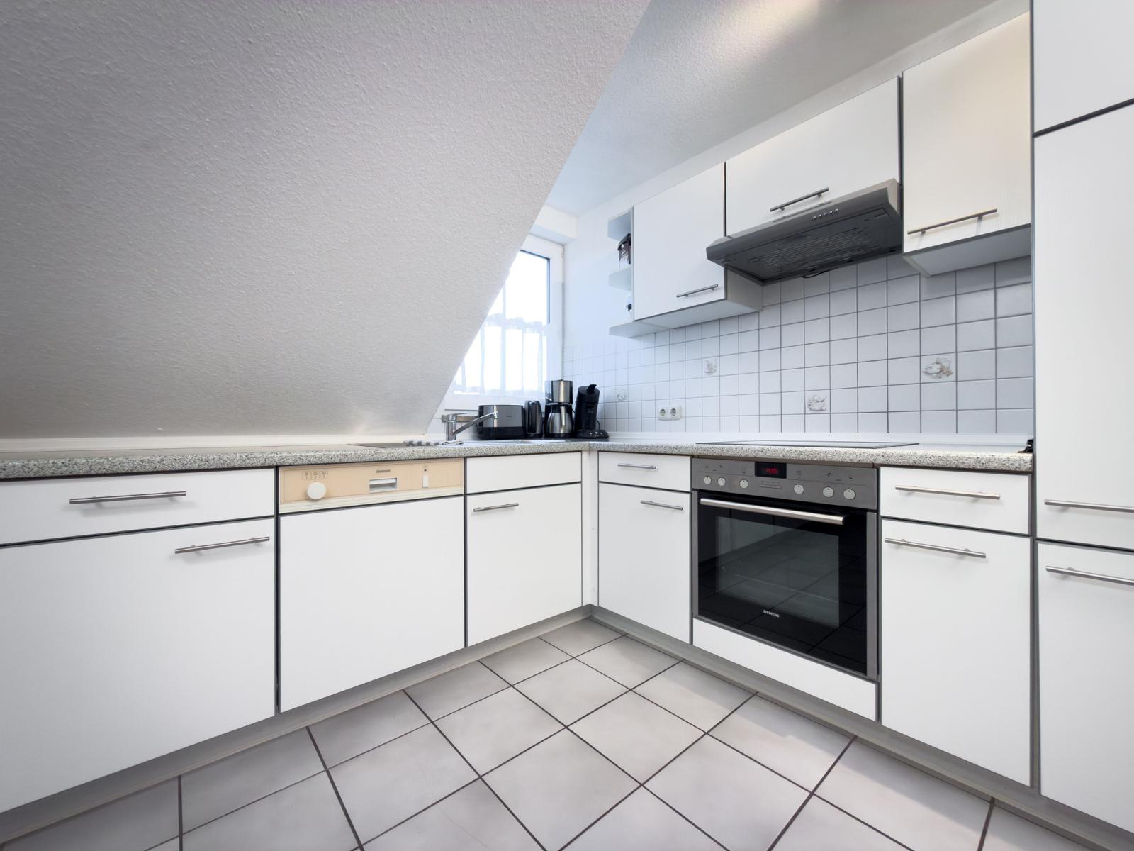 Küche mit weißen Schränken, Edelstahlgeräten und Fliesenboden.