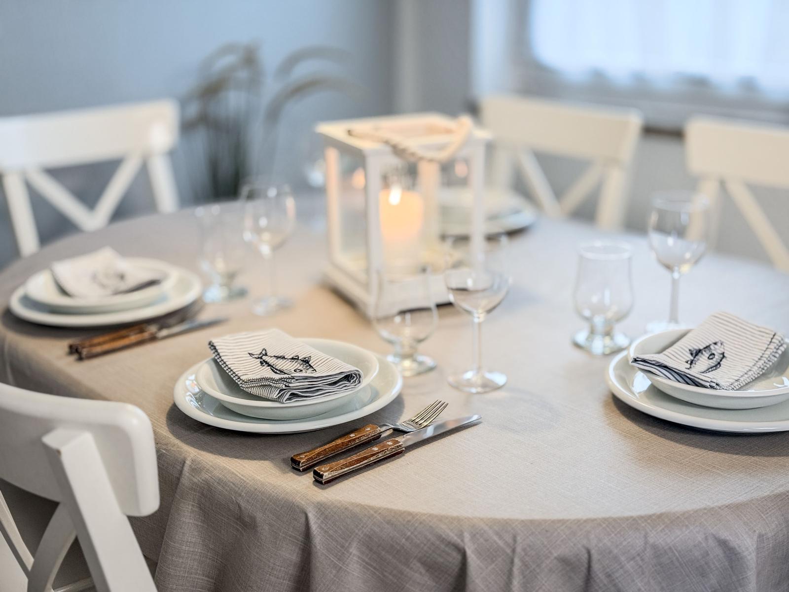 Runde Tisch mit Stühlen, Tischdecke, Geschirr und Kerzenleuchter.