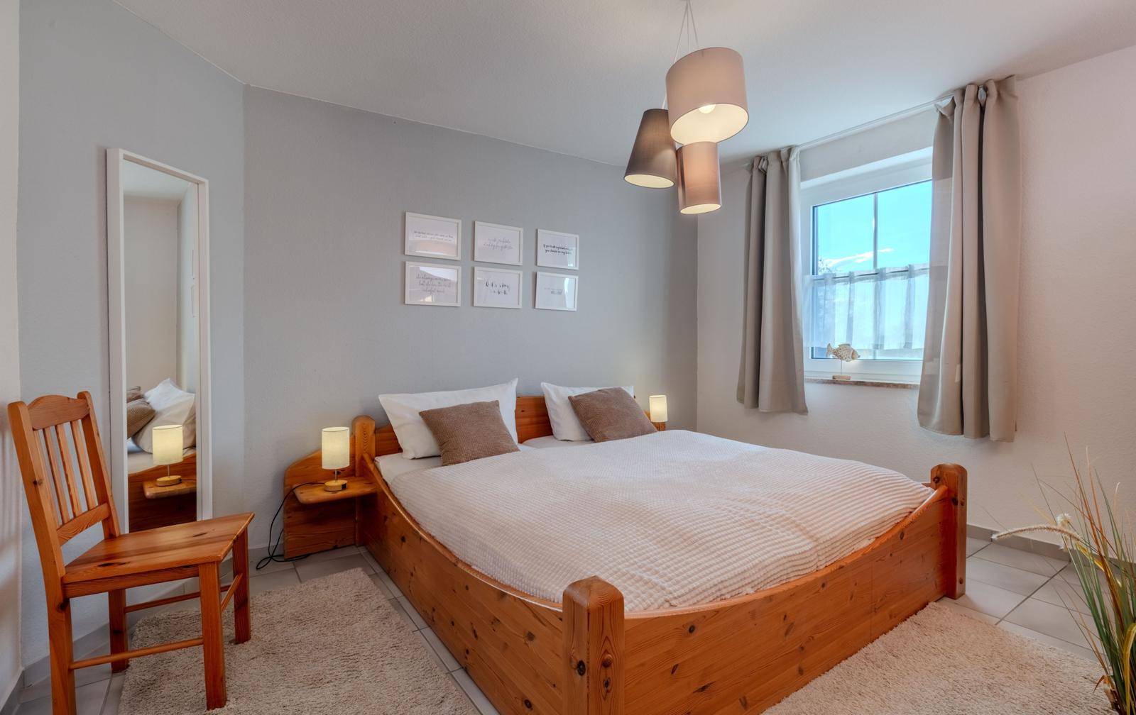 Schlafzimmer mit Holzbett, Fenster und Spiegel.