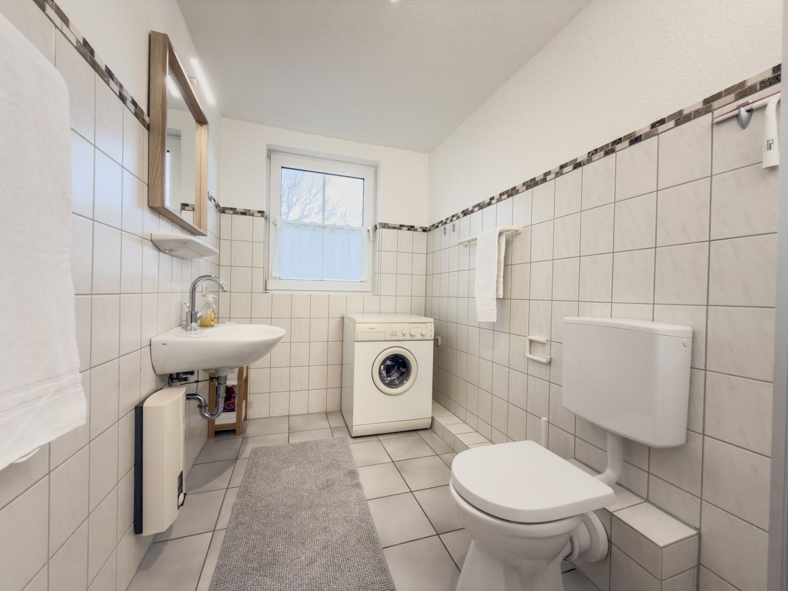 Badezimmer mit Waschmaschine, WC und Spiegel an der Wand.