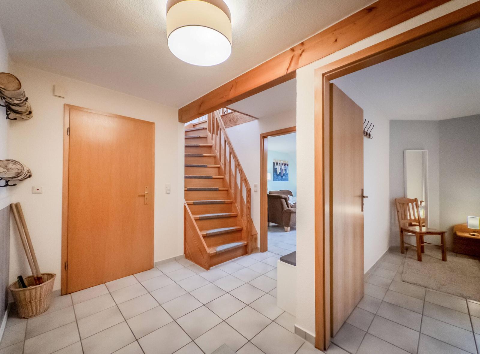 Eingangsbereich mit Holztreppe und Tür. Blick in Wohn- und Schlafzimmer.