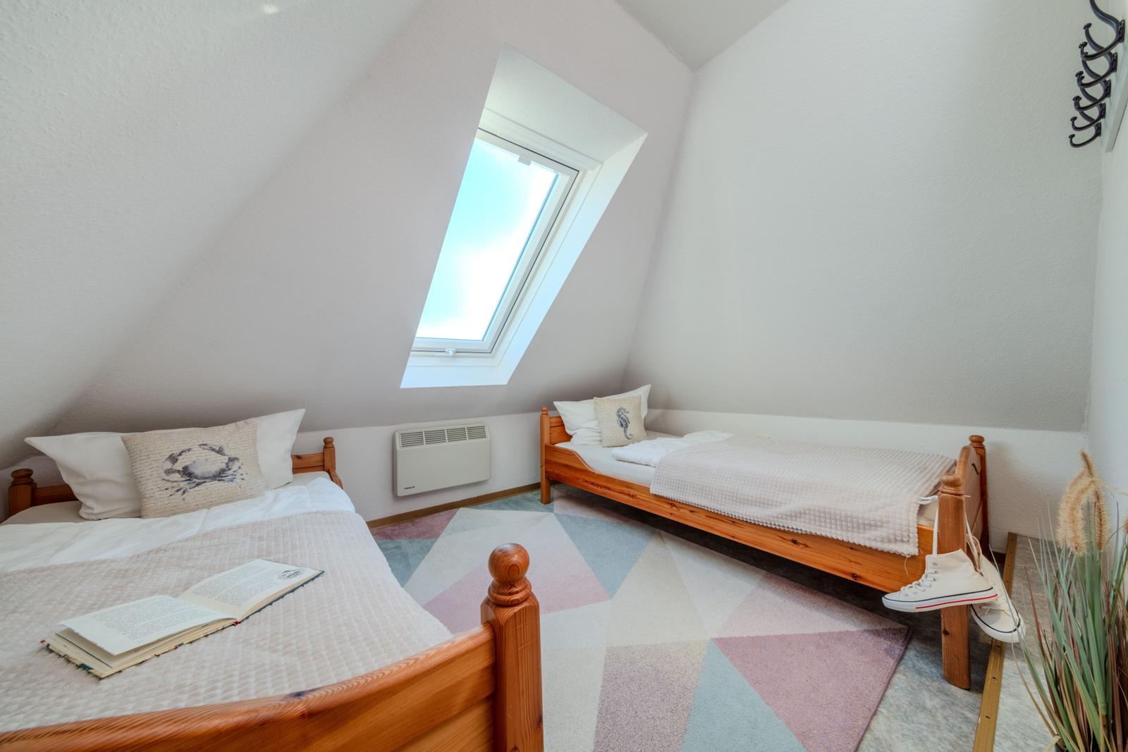 Zwei Betten unter Dachschrägen mit Dachfenster und Teppichboden.