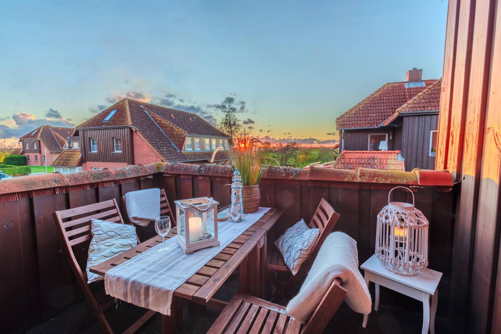 Terrasse mit Tisch, Stühlen und Laterne bei Sonnenuntergang.