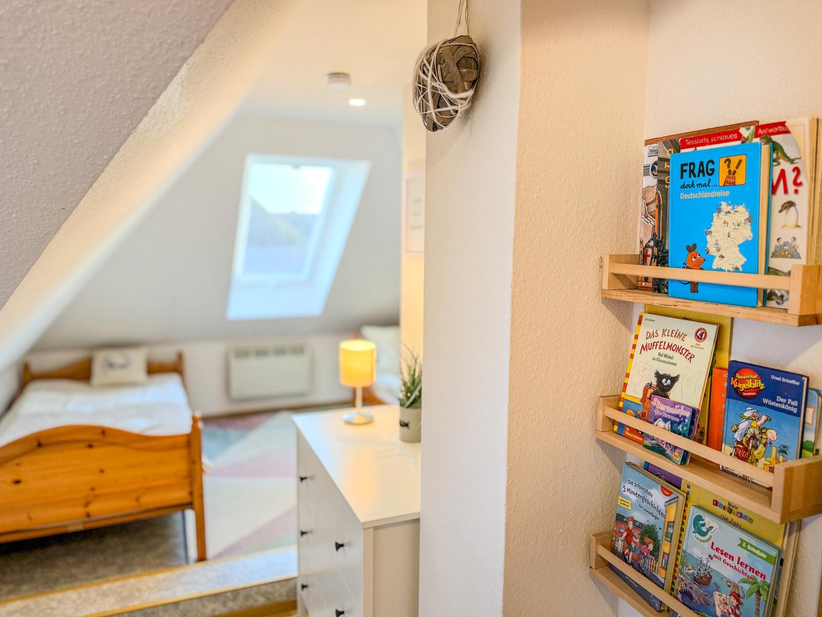 Schlafzimmer mit Dachschrägen und Bücherregal an der Wand.