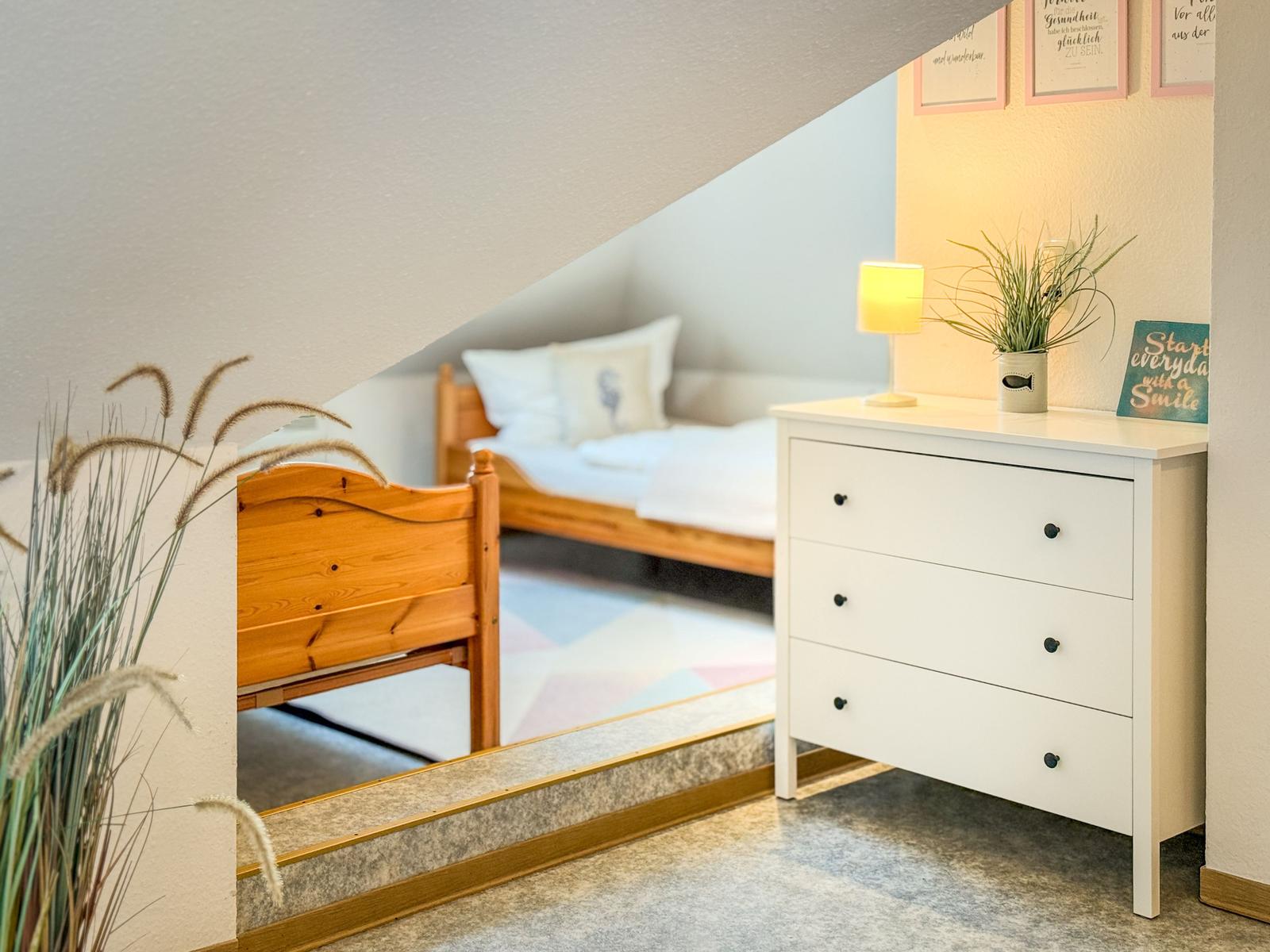 Schlafzimmer mit Holzbett, Schrank und Pflanzen unter Dachschrägen.