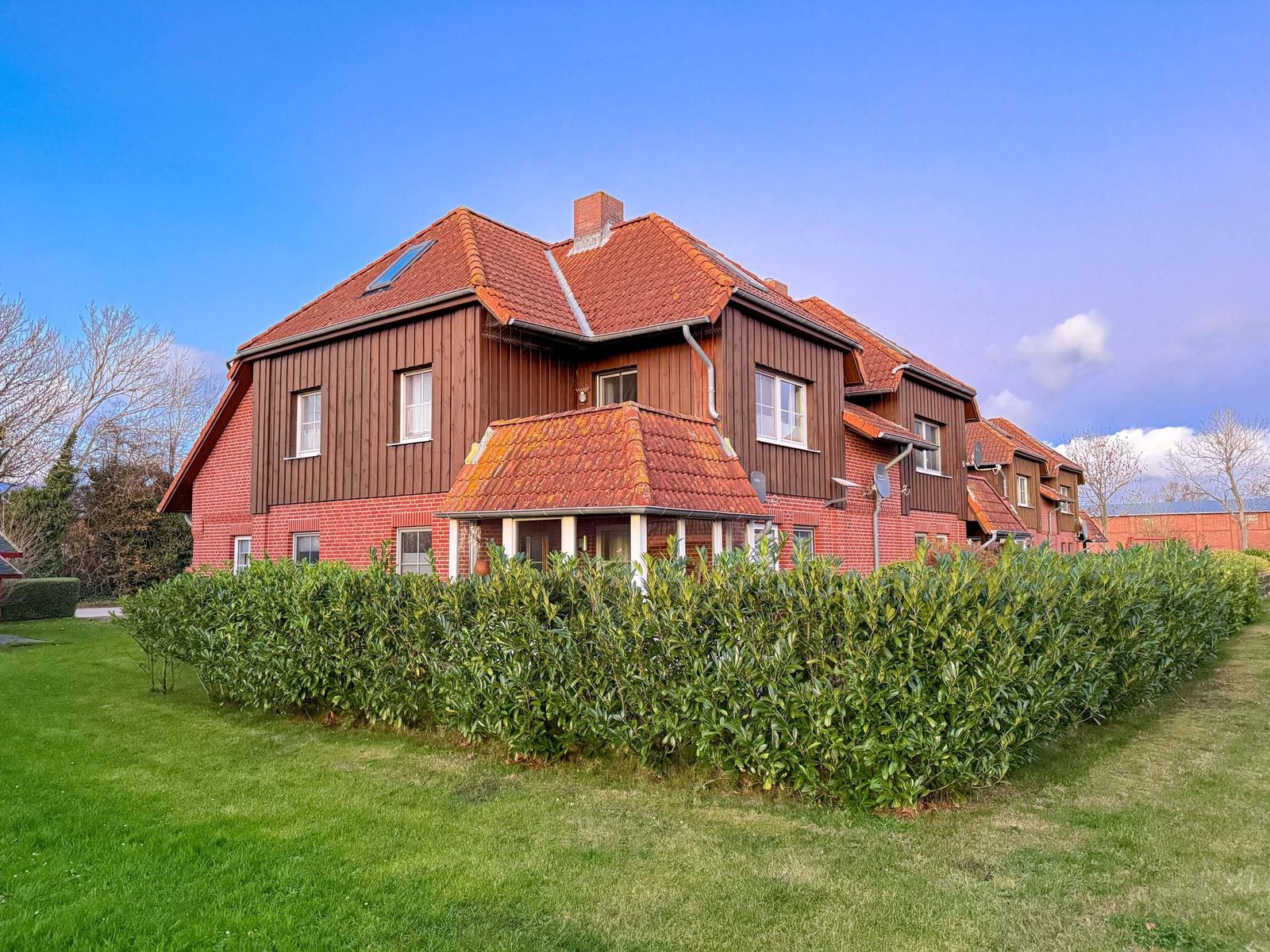 Rotes Doppelhaus mit Holzfassade und Gartenterrasse. Grün bewachsenes Grundstück.