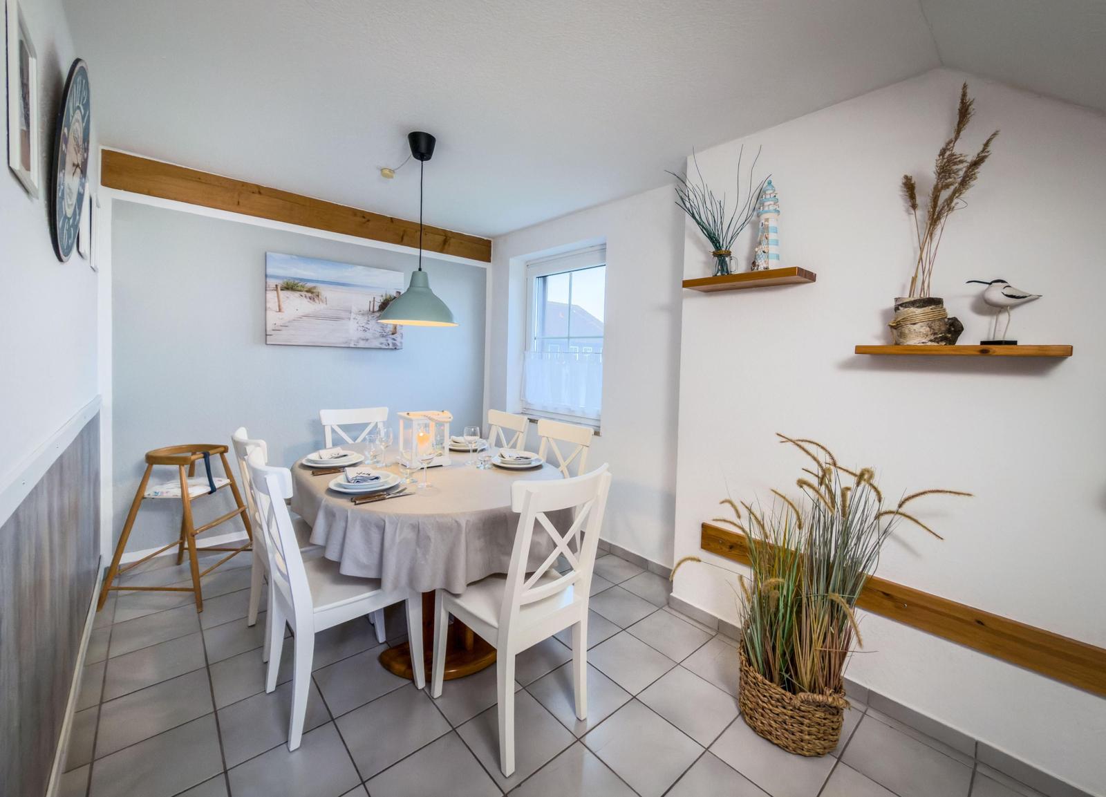 Esszimmer mit runden Tisch, weißen Stühlen und dekorativen Regalen an der Wand.