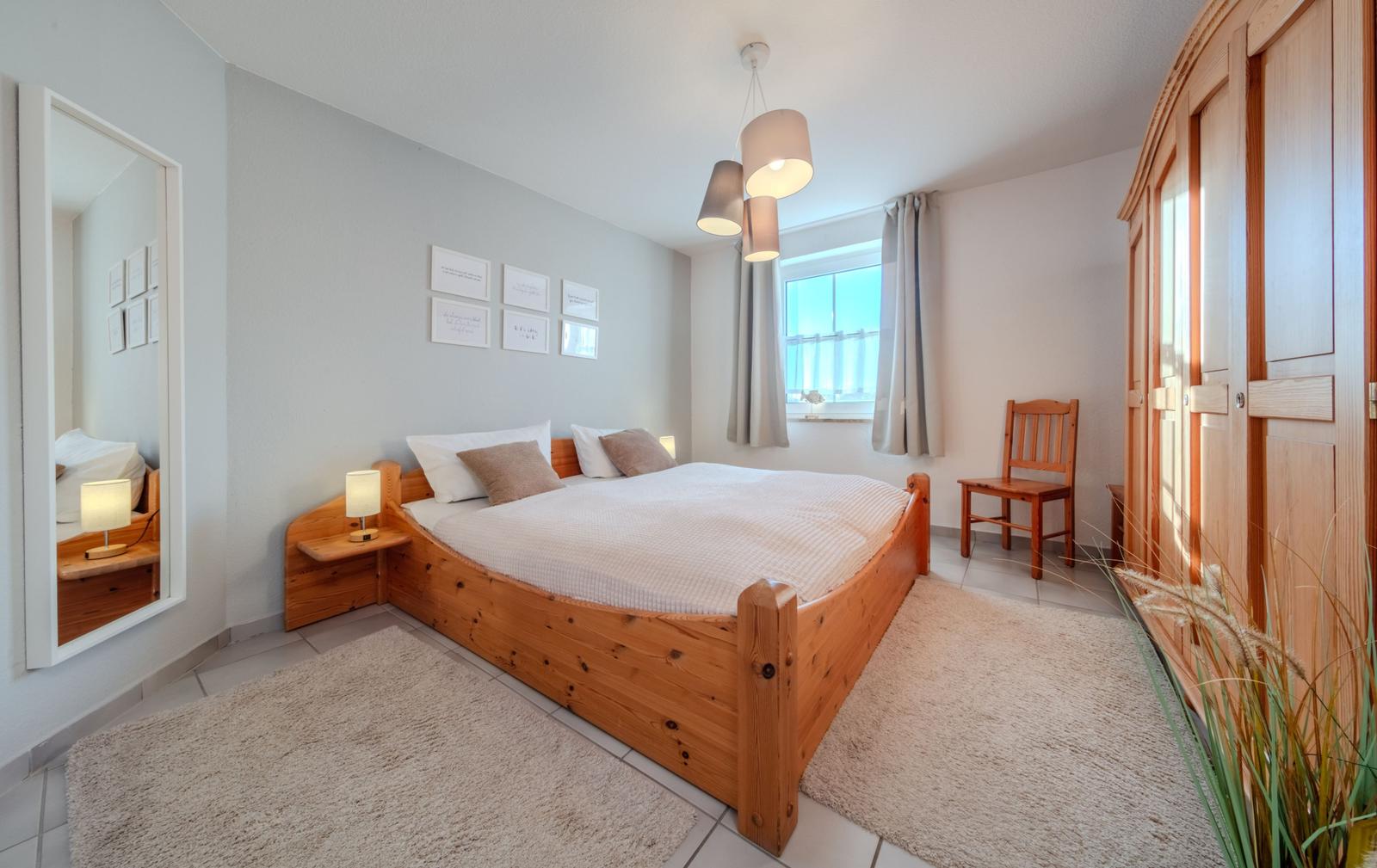 Schlafzimmer mit Holzbett, Spiegel und Kleiderschrank.