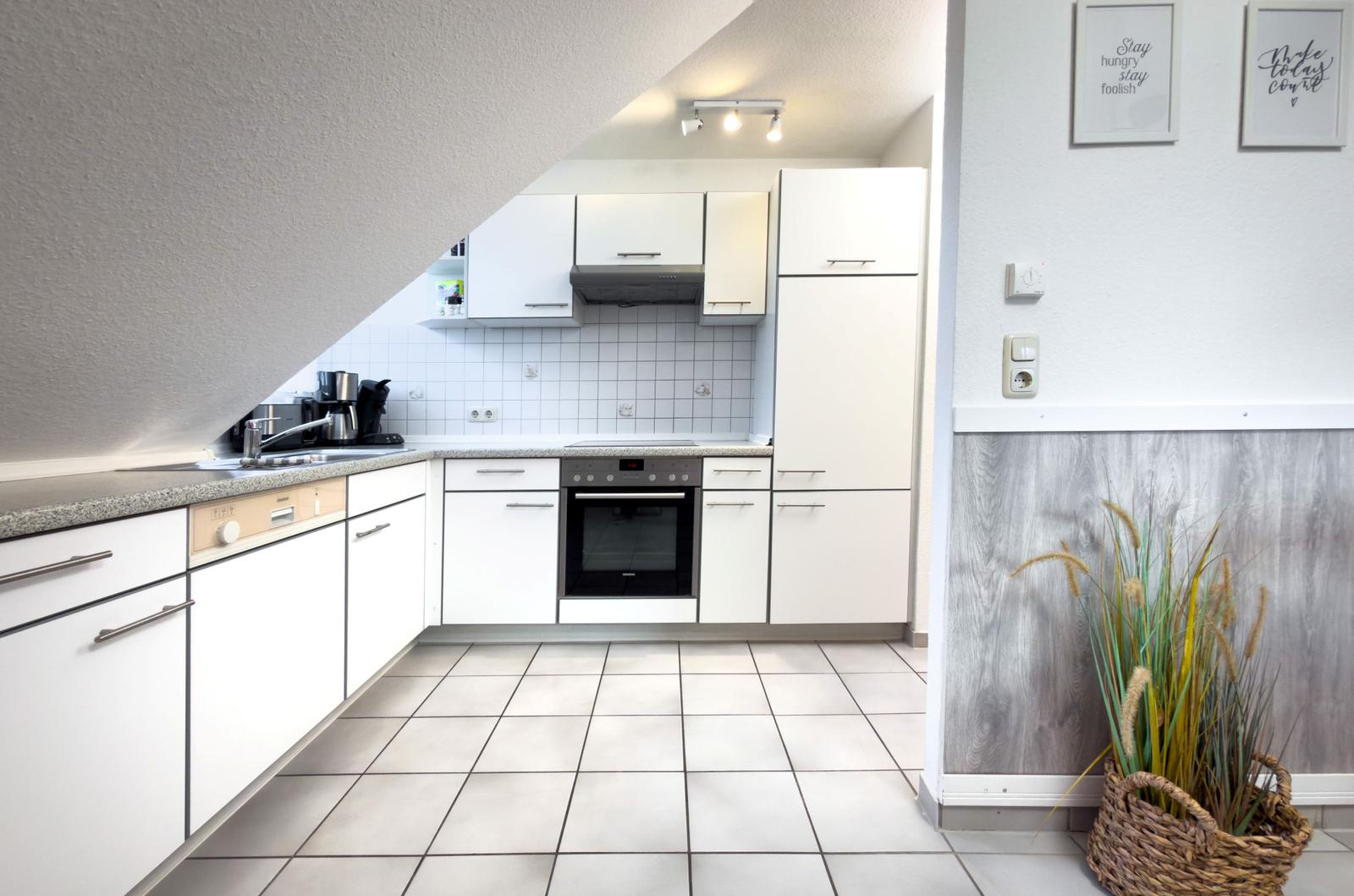 Küche mit weißen Schränken, Edelstahlspüle und integriertem Backofen.