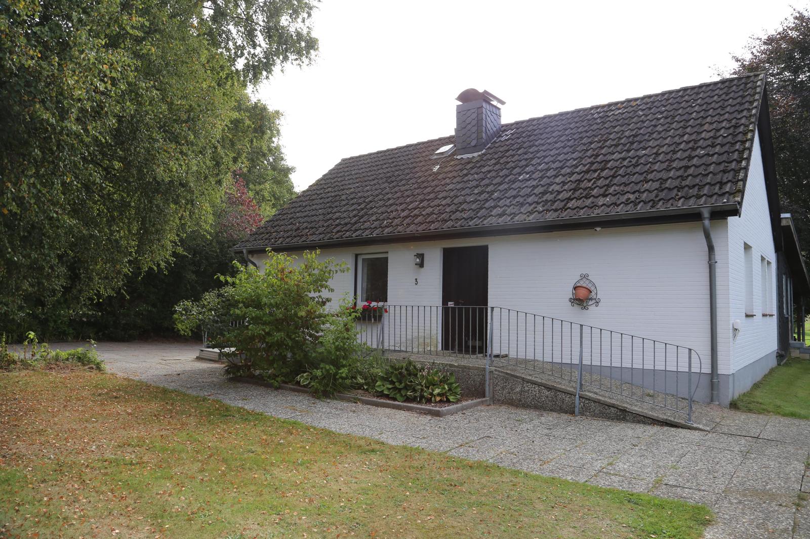 House with white facade, dark roof, and ramp to the entrance door.