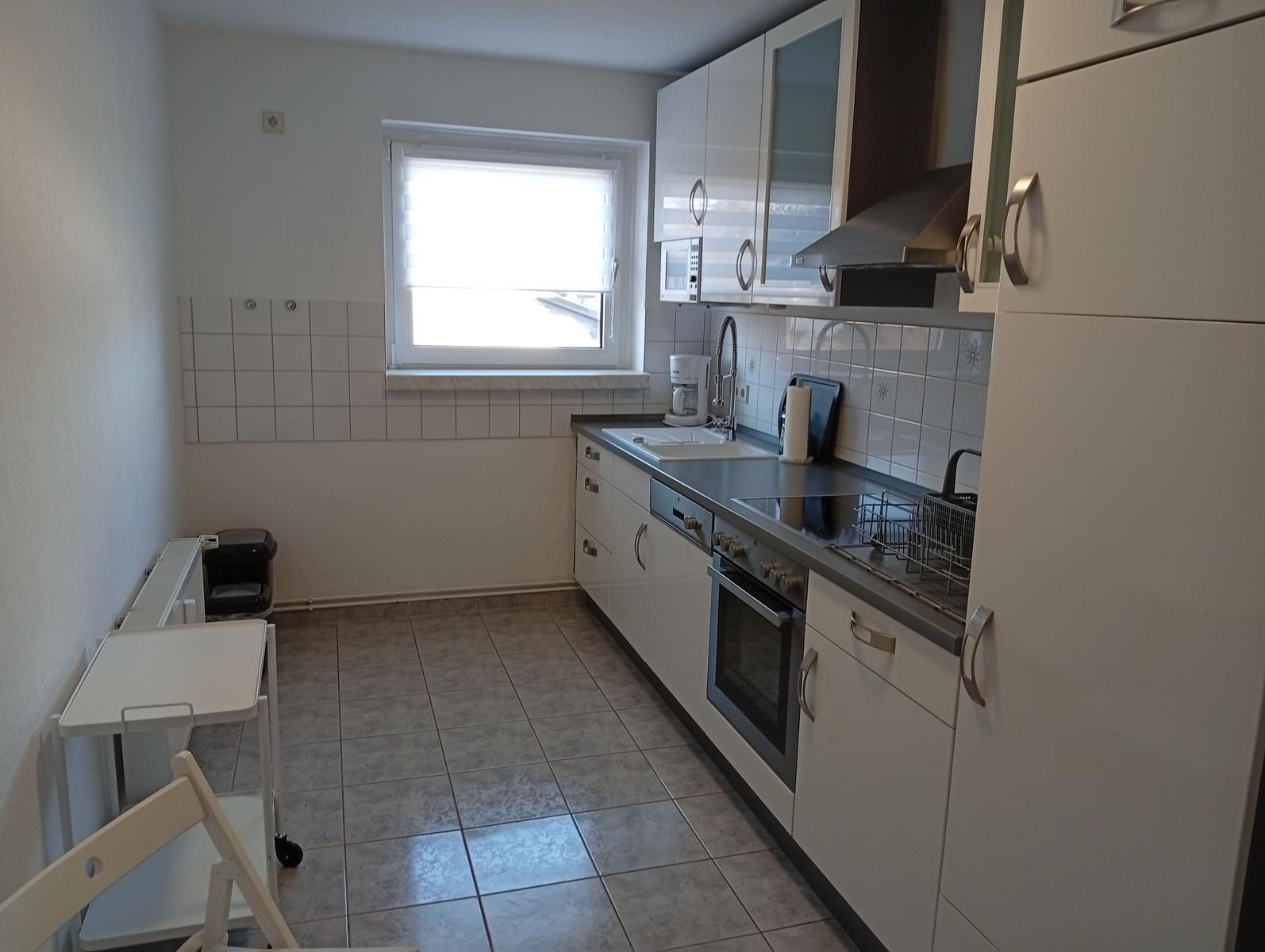 Küche mit weißen Schränken, Herd, Spüle und Fenster.