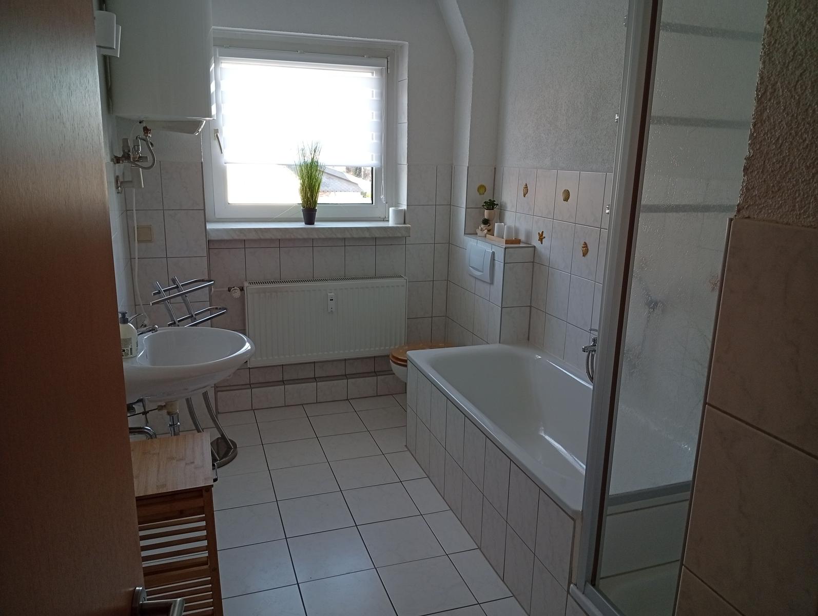 Badezimmer mit Badewanne, Dusche, Waschbecken und Fenster.