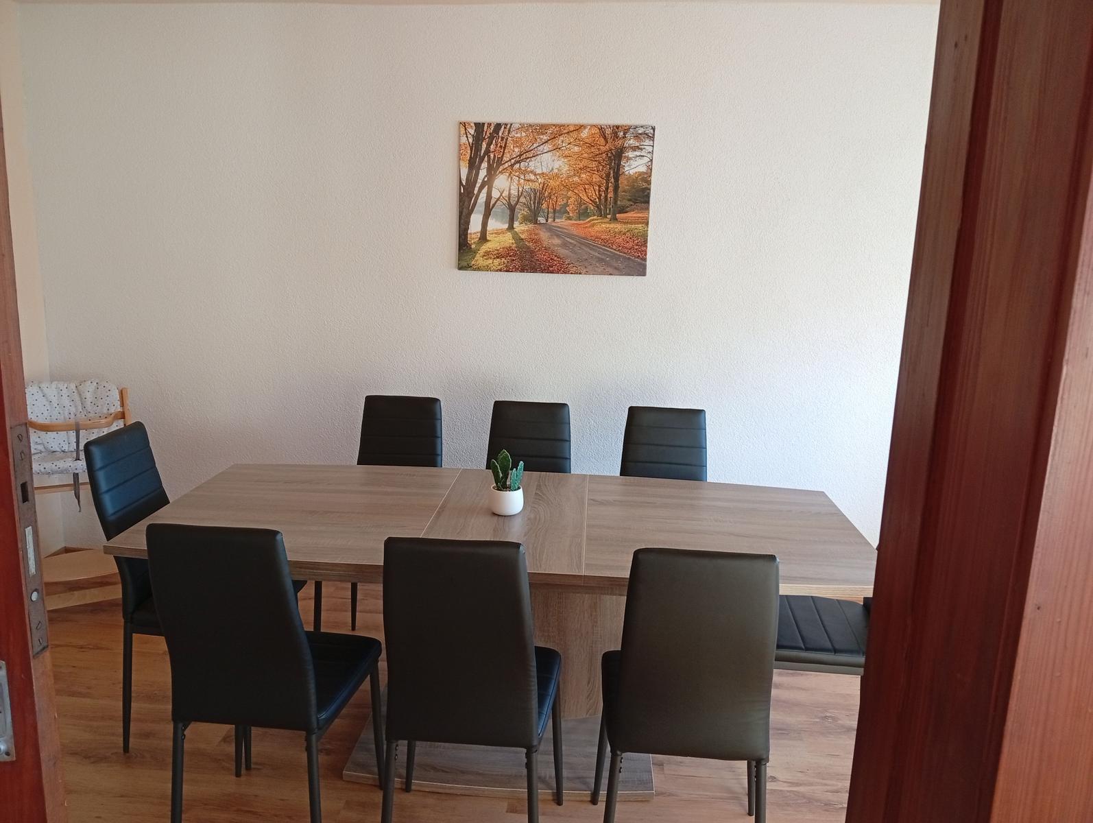 Esszimmer mit Holztisch, sechs Stühlen und Wandbild.