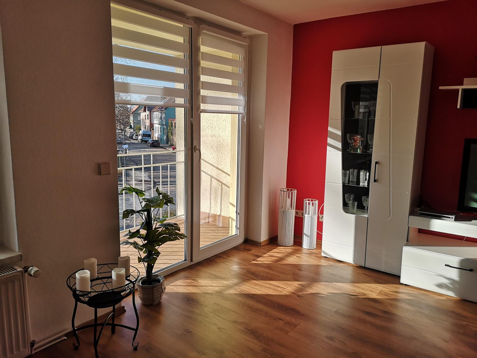 Wohnzimmer mit Blick auf Balkon, rote Wand und weißer Sideboard.