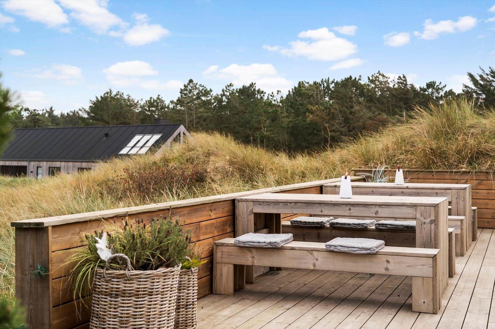 Wooden terrace with benches and cushions, view of forest and sky.