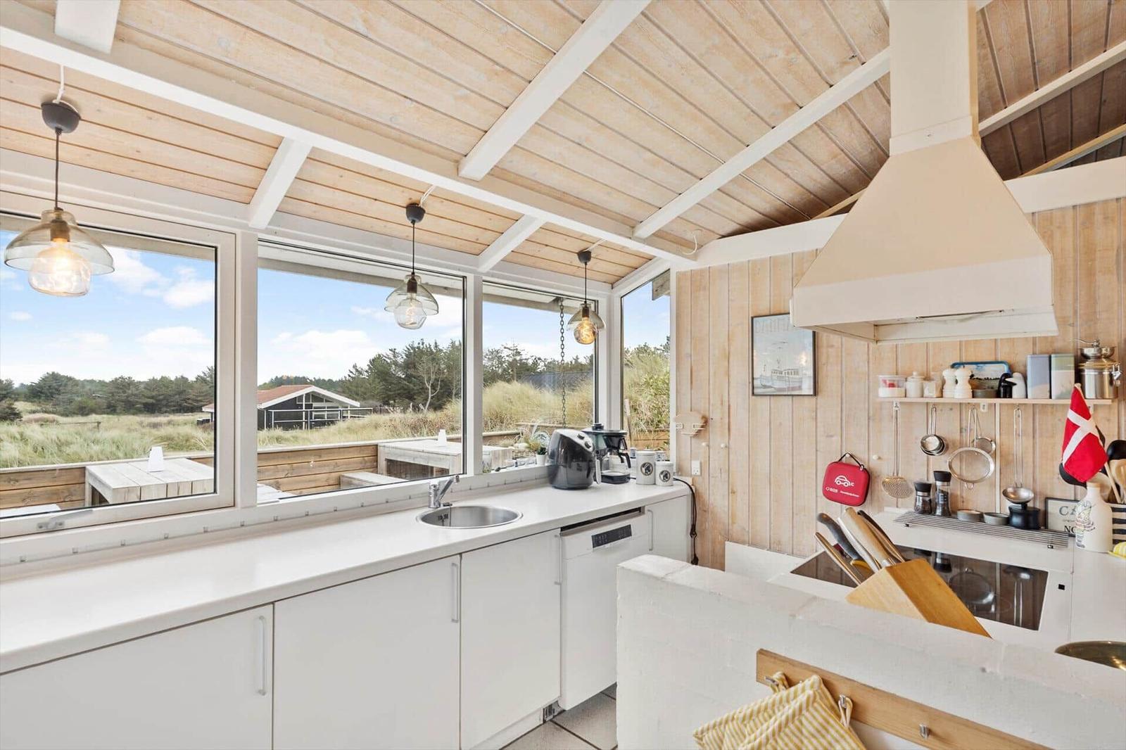 Kitchen with white cabinets, wooden ceiling, and large windows to the garden.