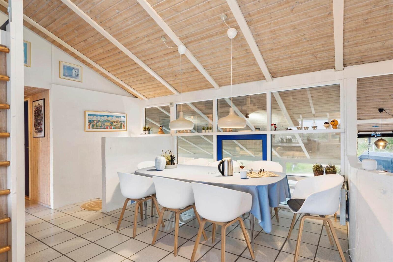 Dining area with white table and chairs under wooden ceiling with white beams.