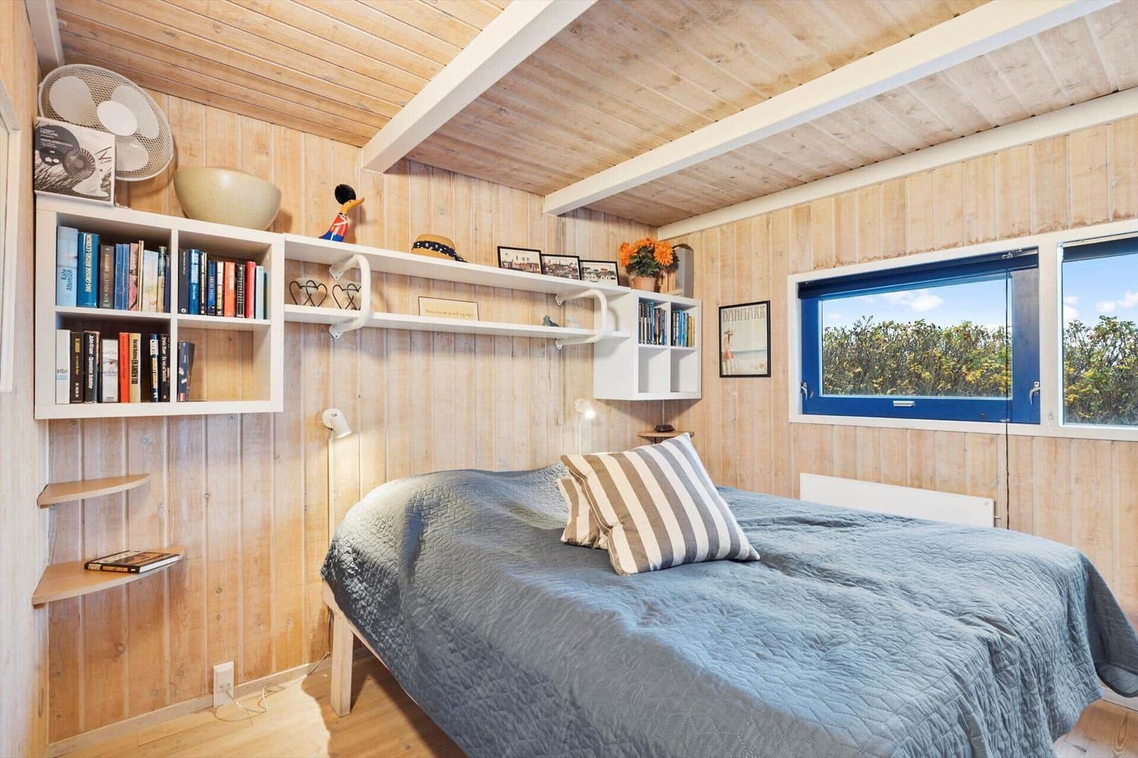 Bedroom with bed, bookshelf, and window with view of greenery.